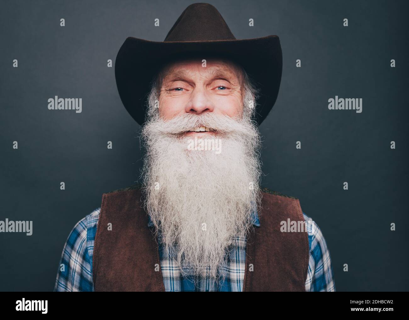 Porträt eines glücklichen bärtigen älteren Mannes mit Cowboyhut Grauer Hintergrund Stockfoto