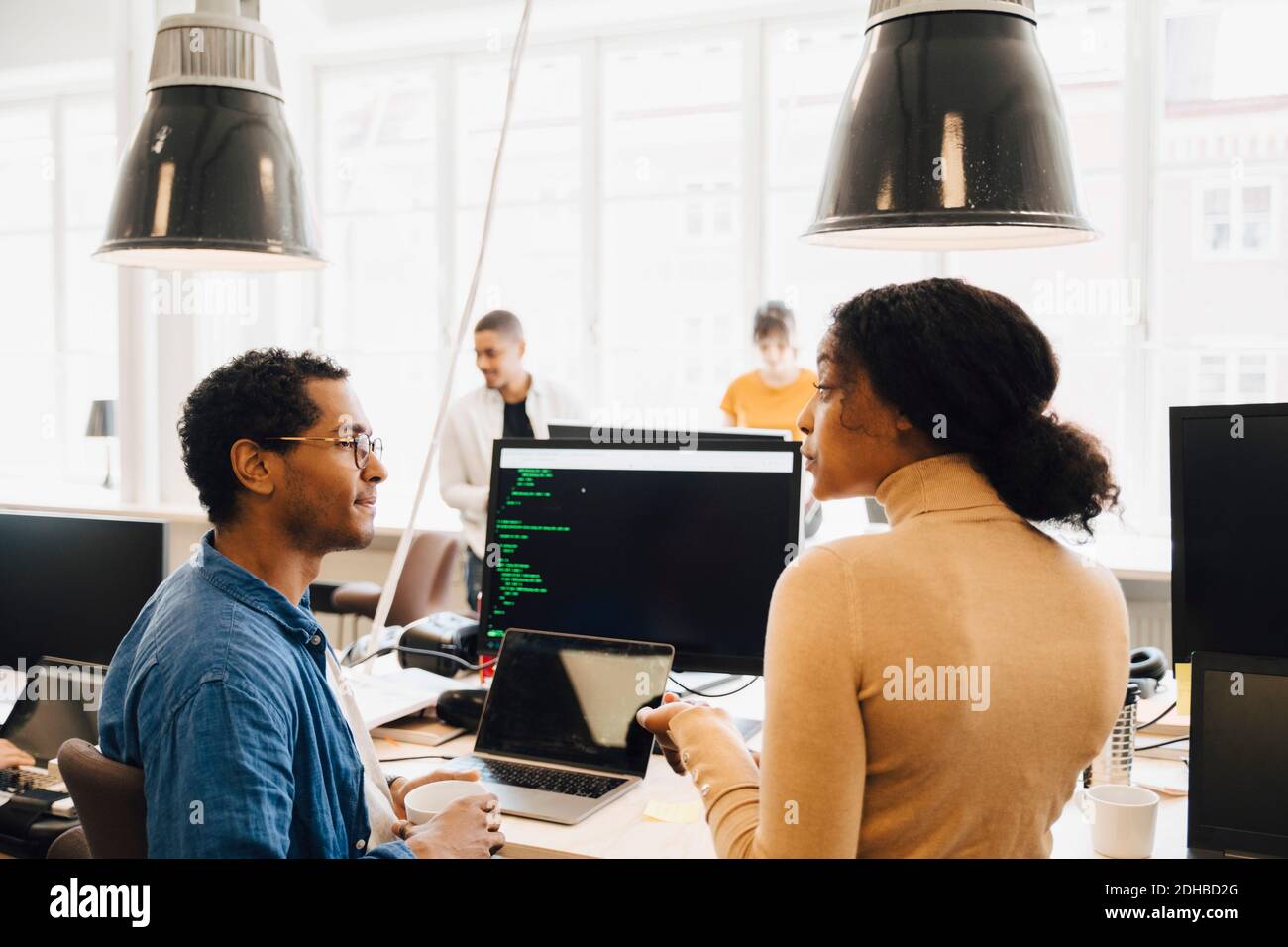 Computerhacker diskutieren am Schreibtisch, während sie im kreativen Büro sitzen Stockfoto