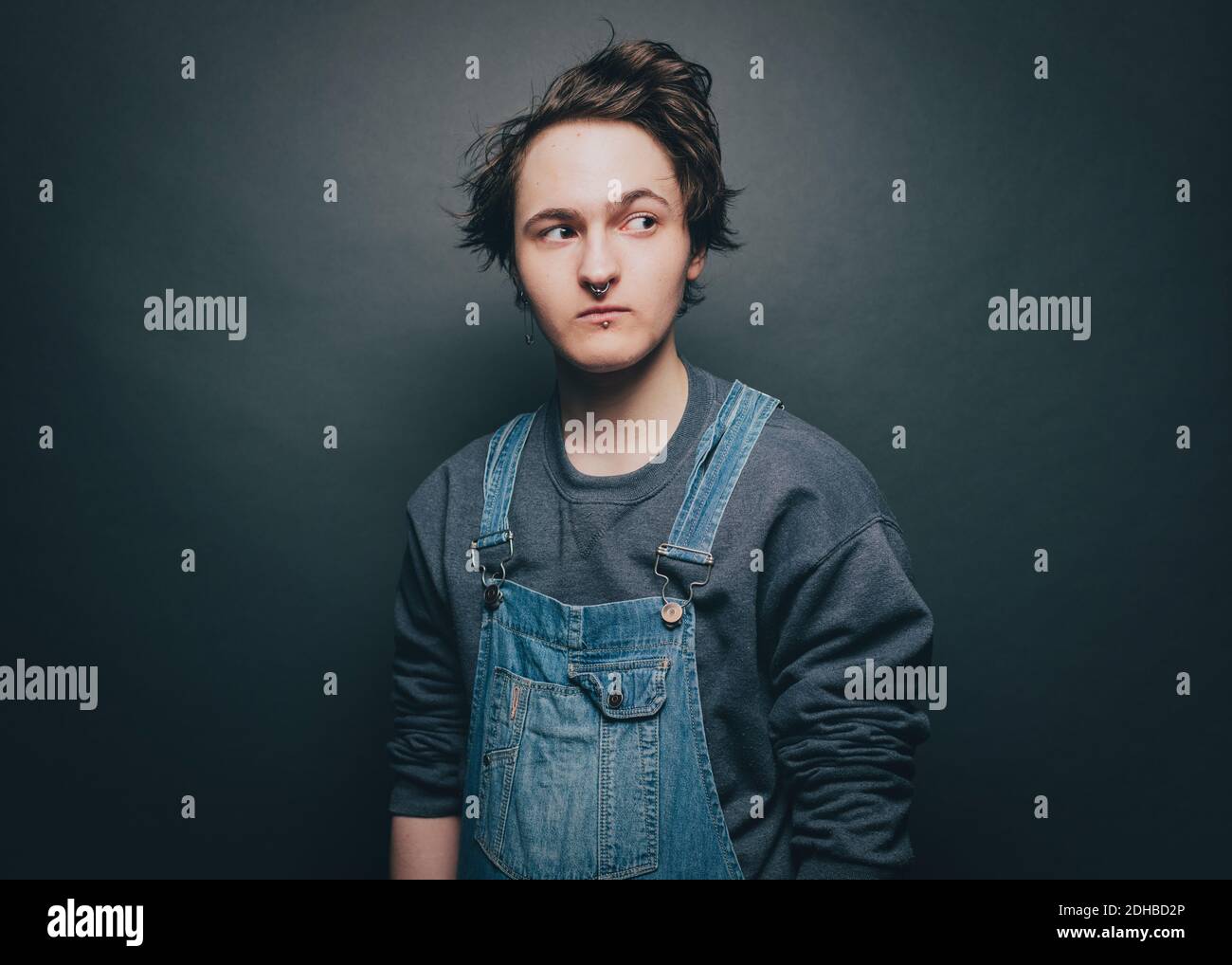 Junger Mann trägt Overalls, während er seitwärts über grauen Hintergrund schaut Stockfoto