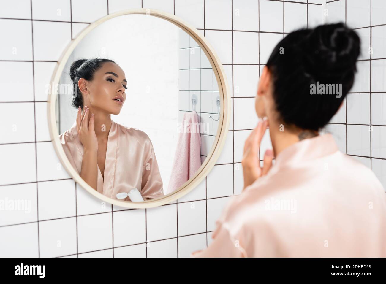 Junge Frau, die kosmetische Creme auf den Hals in der Nähe Spiegel in Badezimmer Stockfoto