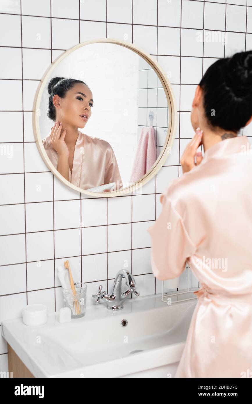 Brunette Frau Anwendung kosmetische Creme in der Nähe Waschbecken und Spiegel Badezimmer Stockfoto