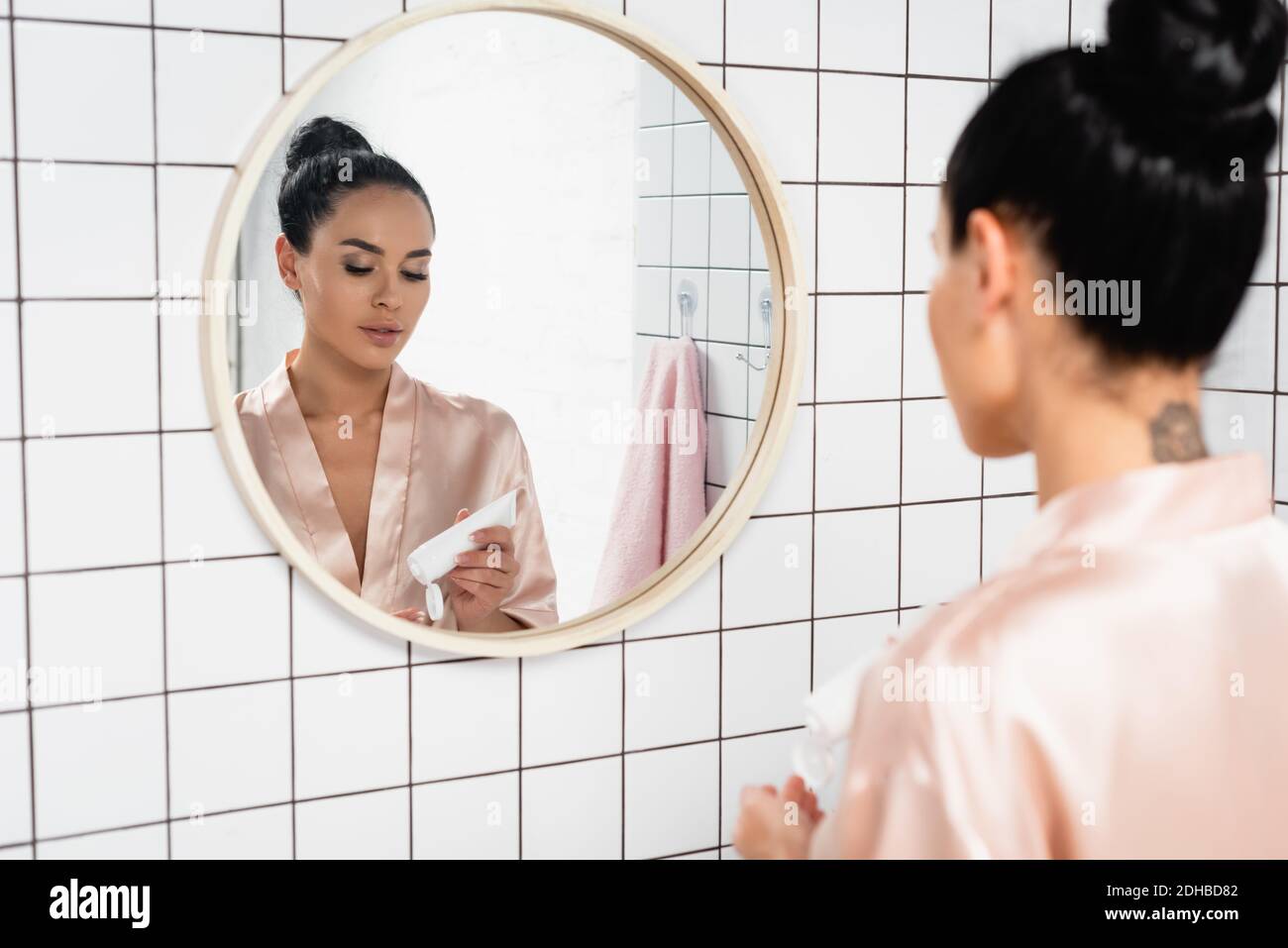 Junge Frau hält Rohr mit kosmetischen Creme in der Nähe Spiegel in Badezimmer Stockfoto