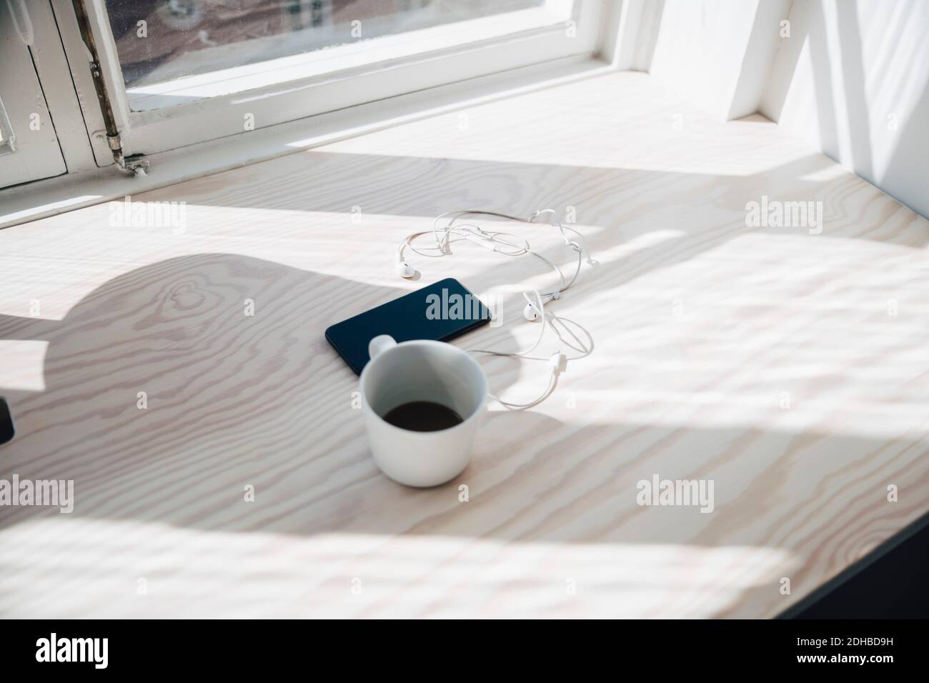 Fernsicht von Smartphone und Kopfhörer mit Kaffee tasse am Schreibtisch am Fenster im Büro Stockfoto