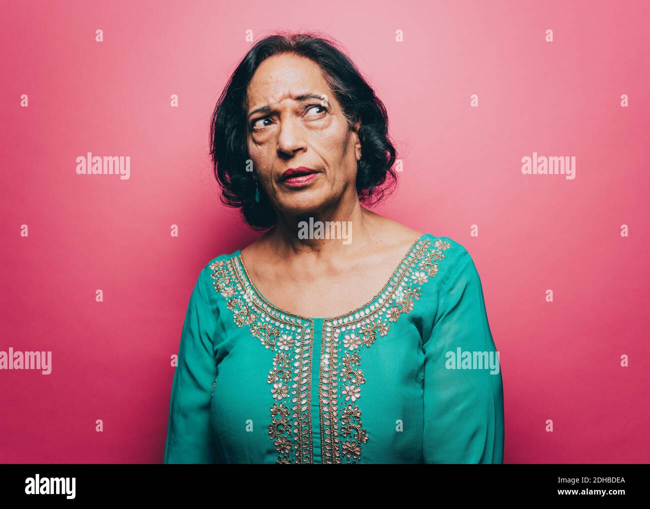 Nachdenkliche ältere Frau, die vor rosa Hintergrund schaut Stockfoto