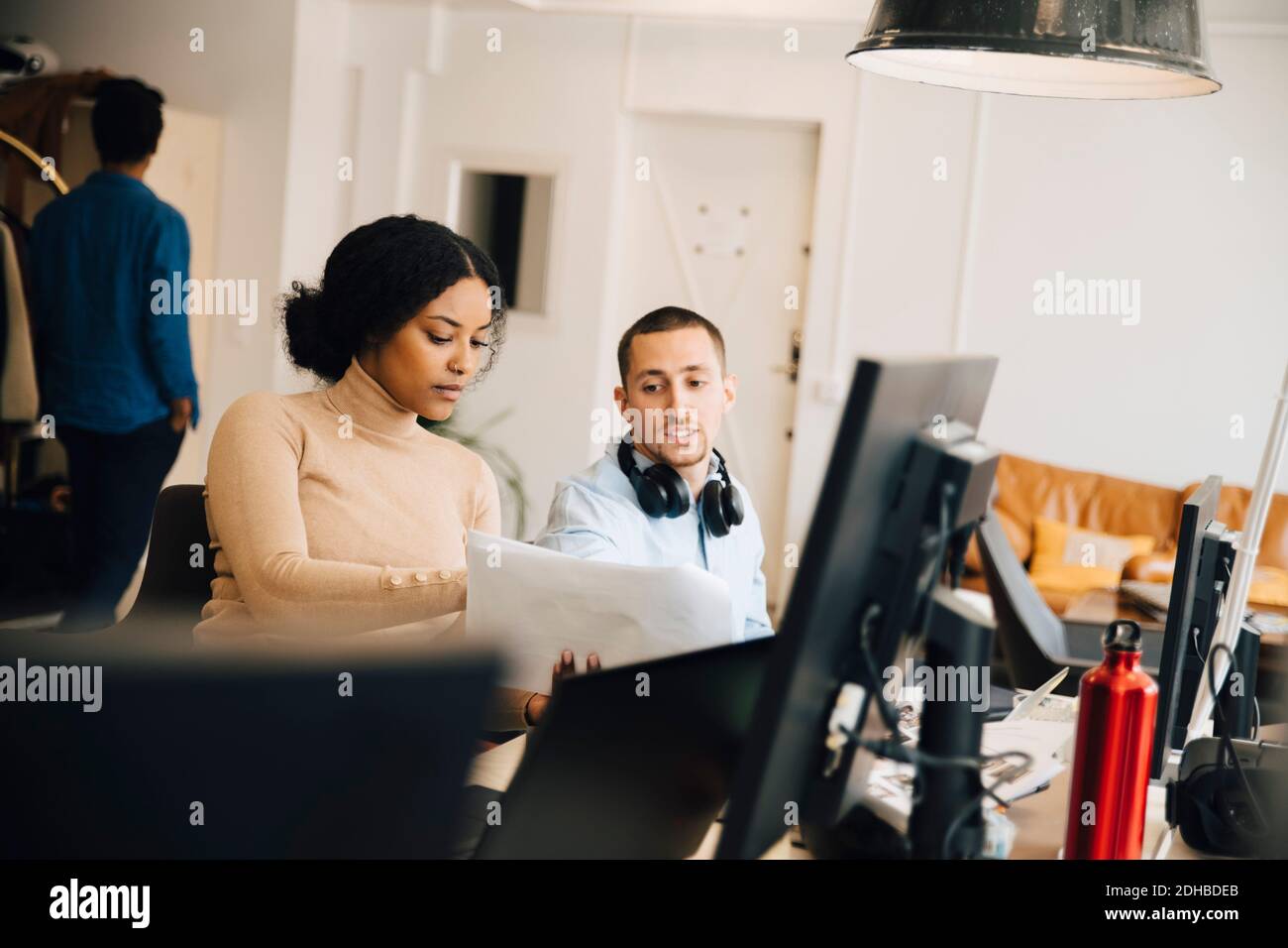 Weibliche Computerhackerin, die dem männlichen Kollegen während des Sitzens ein Dokument vorführt Im Büro Stockfoto