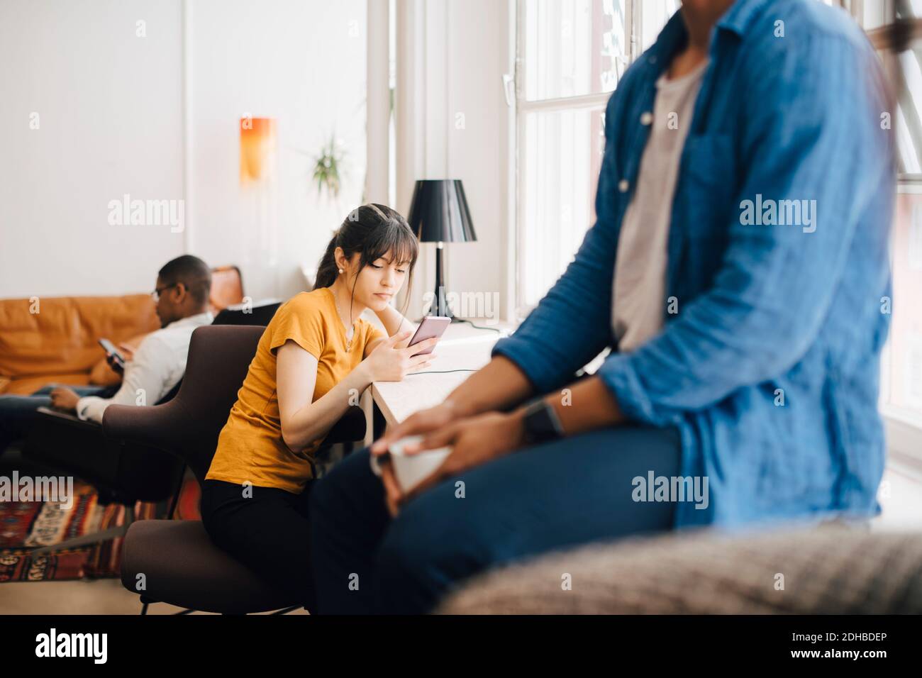 Weibliche Programmiererin mit Mobiltelefon auf dem Schreibtisch, während sie sitzt Büro Stockfoto