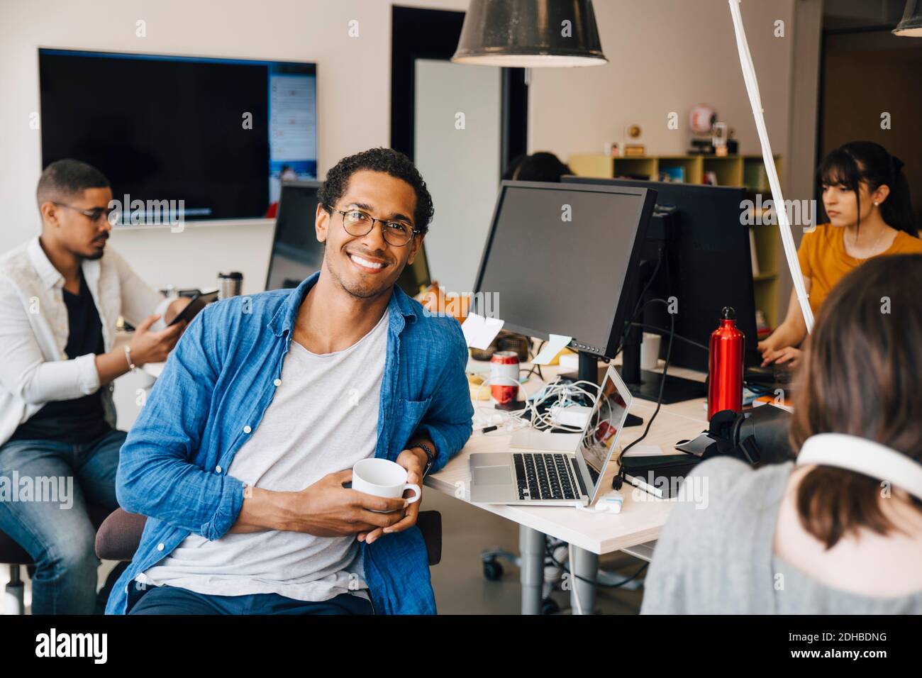 Portrait des männlichen Computerprogrammierers, der von Kollegen am Schreibtisch sitzt Im Büro Stockfoto
