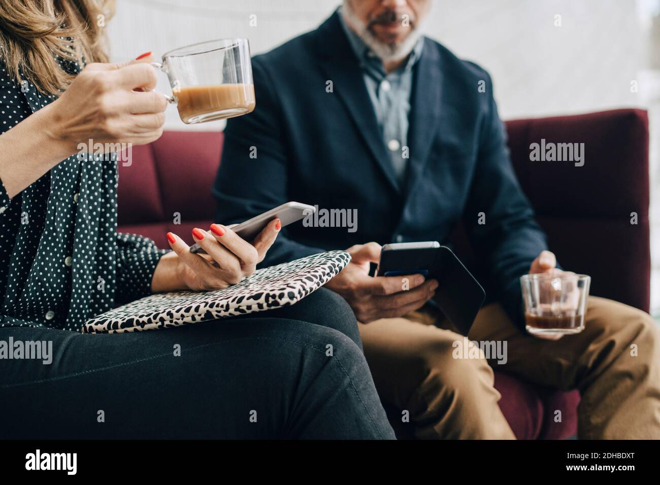 Mittelteil von Geschäftsleuten, die Mobiltelefone benutzen und Tee trinken Auf dem Tisch während der Konferenz Stockfoto