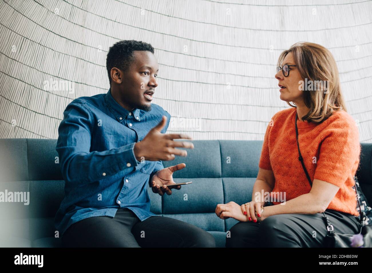 Geschäftsmann teilt Ideen mit einer Kollegin, während sie auf der Couch sitzt Bei der Konferenz Stockfoto