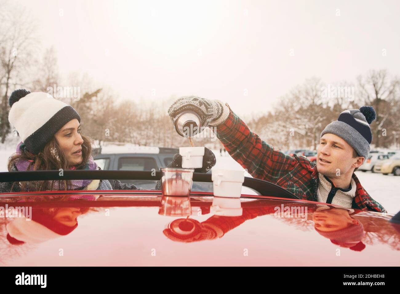 Freund, der den Mann ansieht, der Kaffee in der Tasse über das Auto gießt Haube Stockfoto