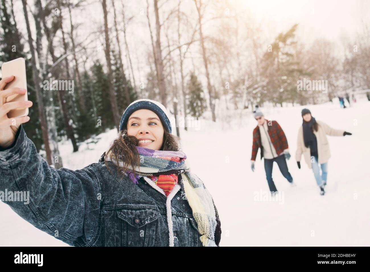 Lächelnde Frau, die Selfie nimmt, während Freunde im Hintergrund laufen Stockfoto