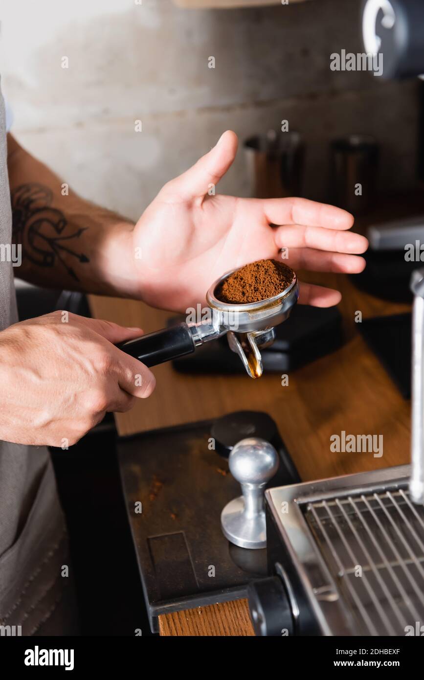 Beschnittene Ansicht des tätowierten Barista, der Portafilter mit geröstetem Boden hält Kaffee Stockfoto