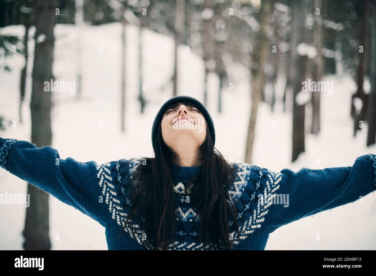 Glückliche Frau, die während des Aufstehens mit den Armen auf dem schneebedeckten Feld steht Winter Stockfoto
