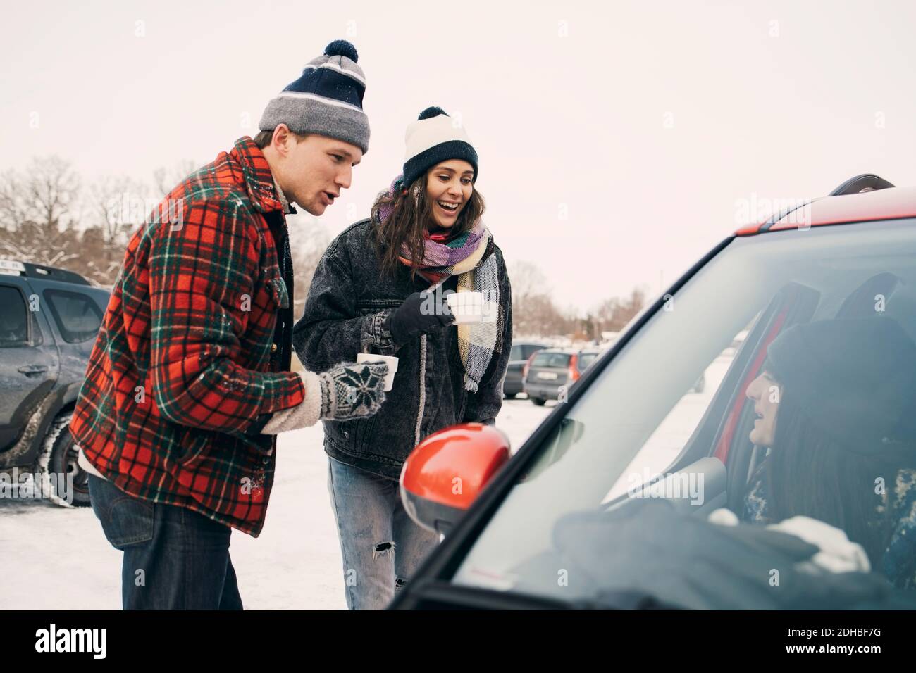 Glücklicher Mann und Frau, die Kaffee trinken, während sie mit einem Freund sprechen Im Winter im Auto sitzen Stockfoto