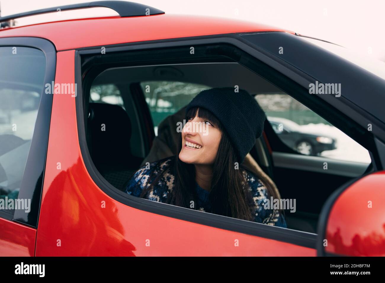 Lächelnde Frau schaut weg, während sie im roten Auto sitzt Stockfoto
