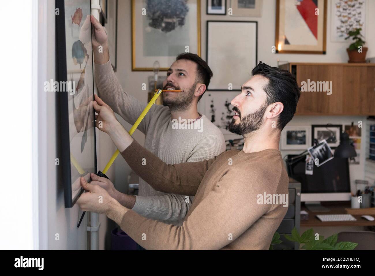 Junger Mann mit Band Maßnahme Partner beim Aufhängen Malerei unterstützen An der Wand Stockfoto