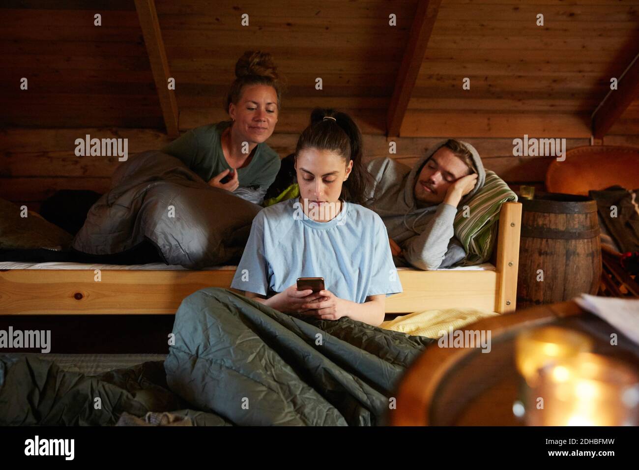 Freunde, die Frauen mit dem Smartphone betrachten, während sie sich entspannen Bett in der Hütte Stockfoto