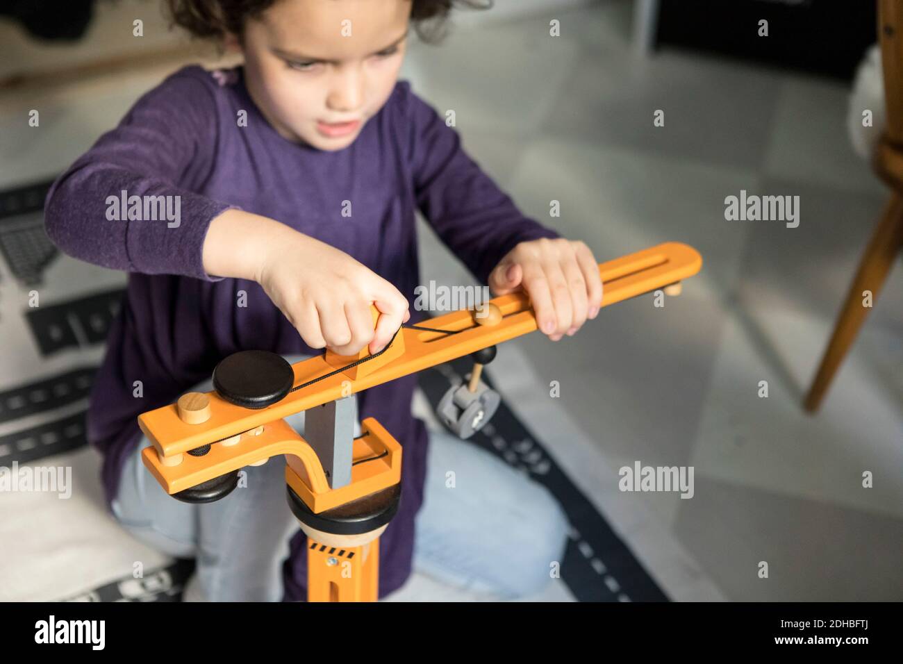 High-Winkel-Ansicht von Mädchen spielen mit Kran Spielzeug auf Boden zu Hause Stockfoto