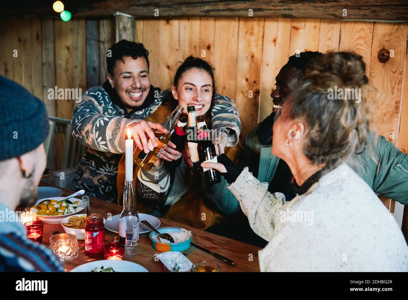Fröhliche Männer und Freunde, die Bierflaschen beim Sitzen toasten Blockhütte Stockfoto