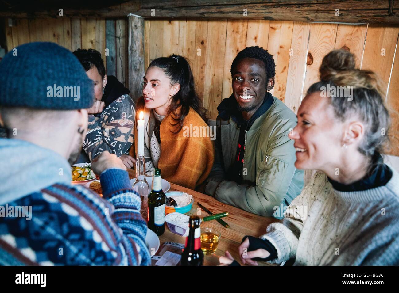 Porträt eines jungen Mannes, der mit Freunden im Gespräch sitzt Essen in der Blockhütte Stockfoto