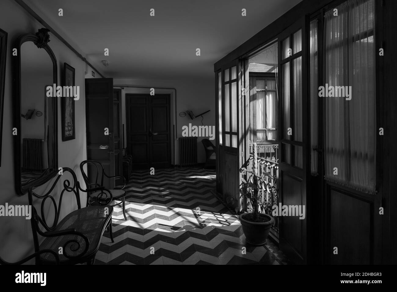 Eine Graustufenaufnahme des Flurs mit Spiegel, Bank, Kleiderschrank und Türen, die zum Balkon führen Stockfoto