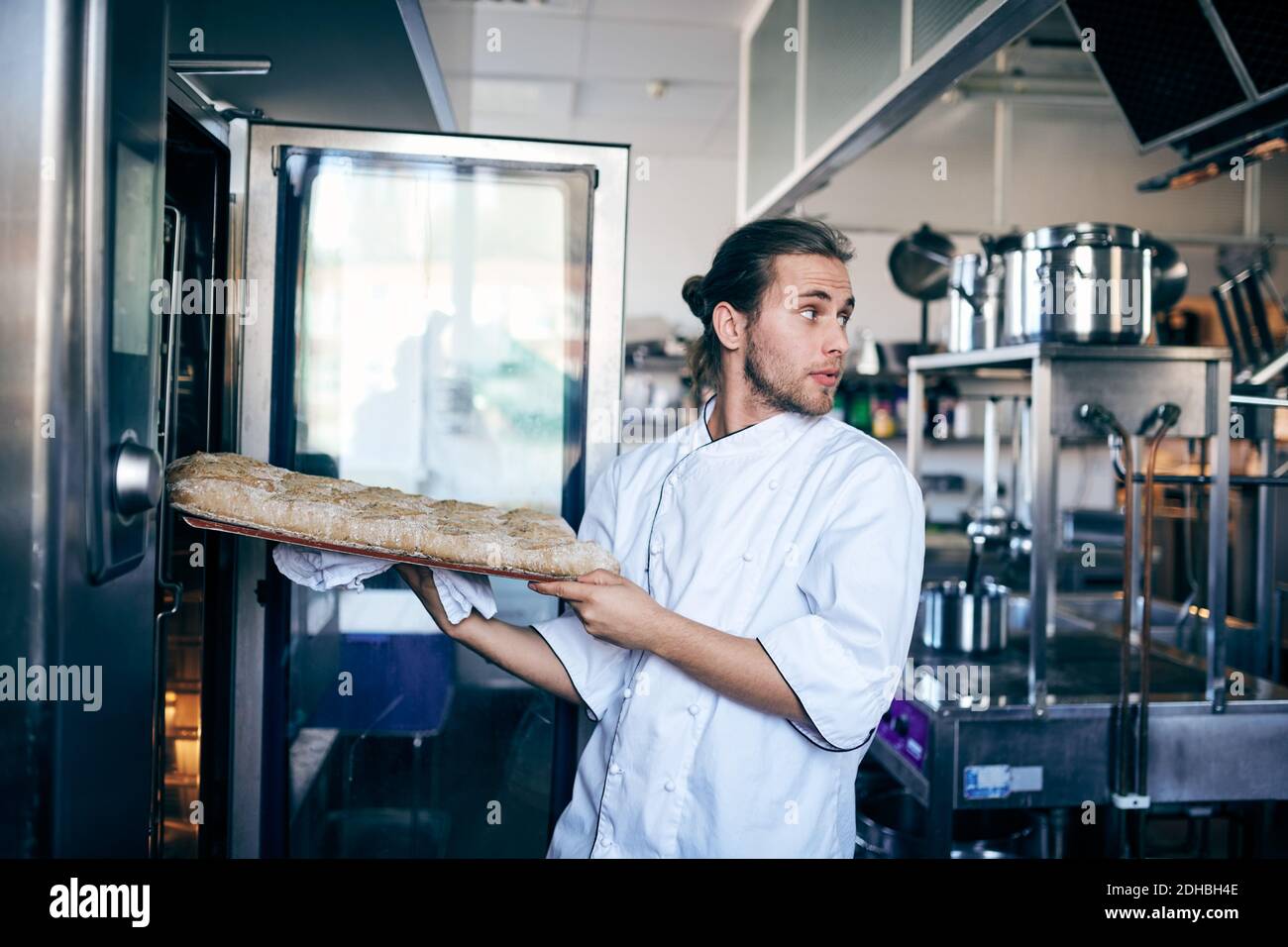 Männlicher Koch, der Brot in den Ofen legt, während er wegschaut Gewerbliche Küche Stockfoto