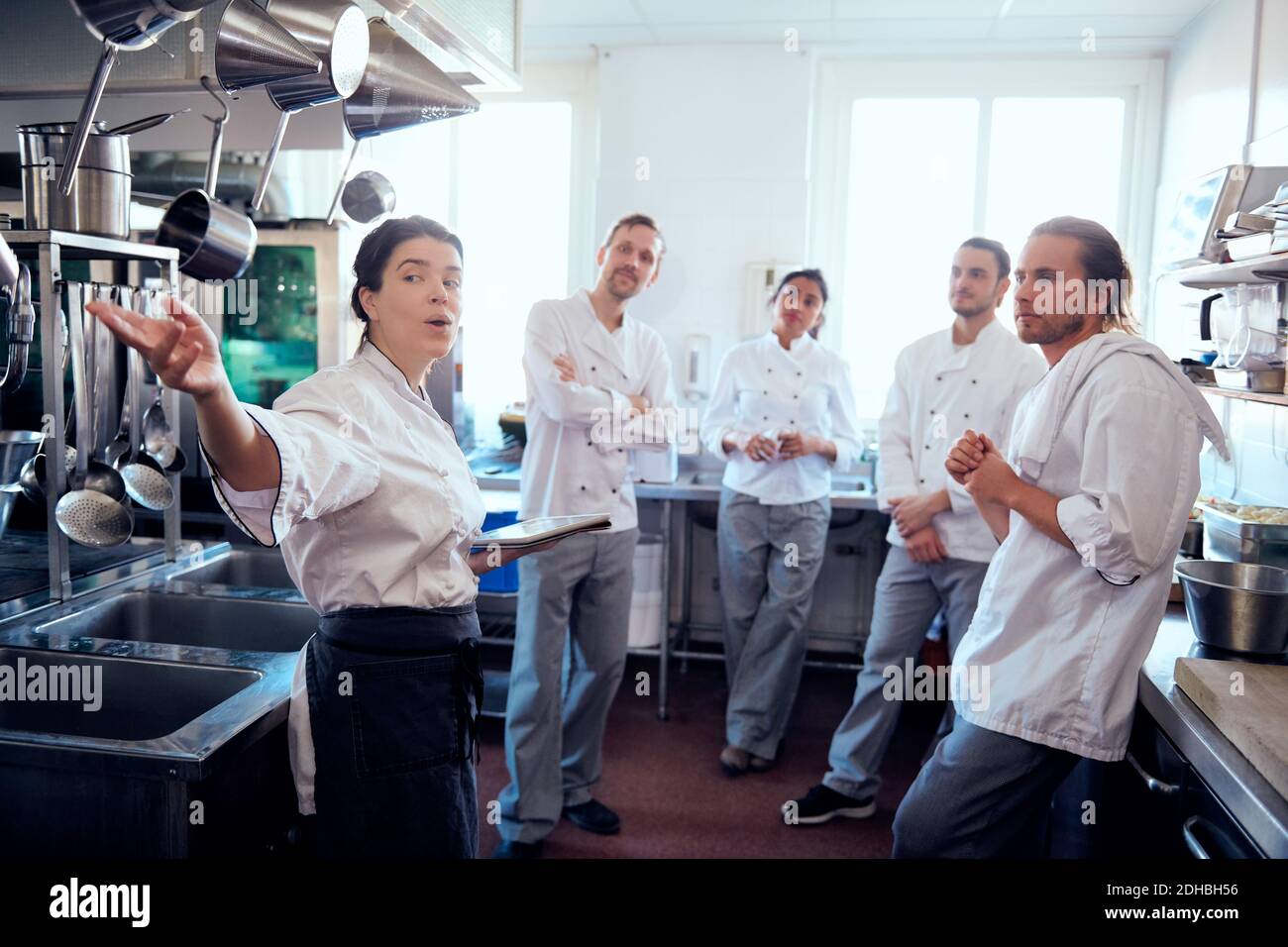 Köchin mit mittlerem Erwachsenenalter und digitalem Tablet mit Kollegen diskutieren In der kommerziellen Küche Stockfoto