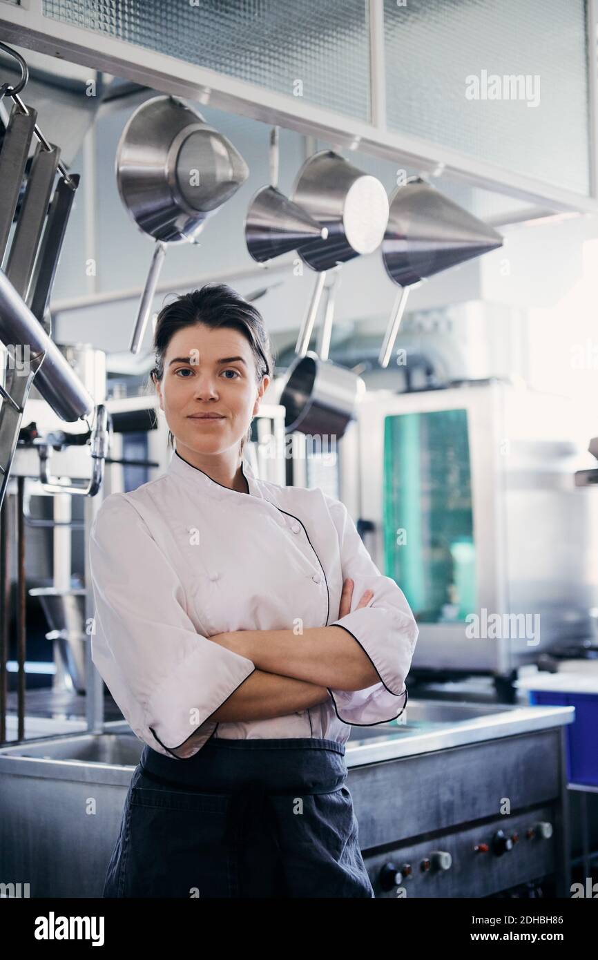 Porträt einer Köchin mit mittleren Erwachsenen, die die Arme gekreuzt hat Gewerbliche Küche Stockfoto