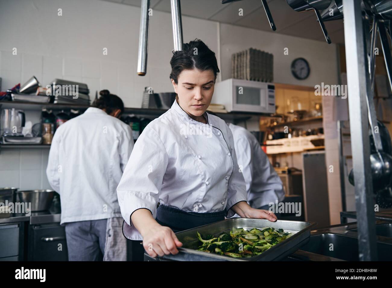 Mittlere Erwachsene weibliche Köchin hält Backblech mit Brokkoli an Gewerbliche Küche Stockfoto