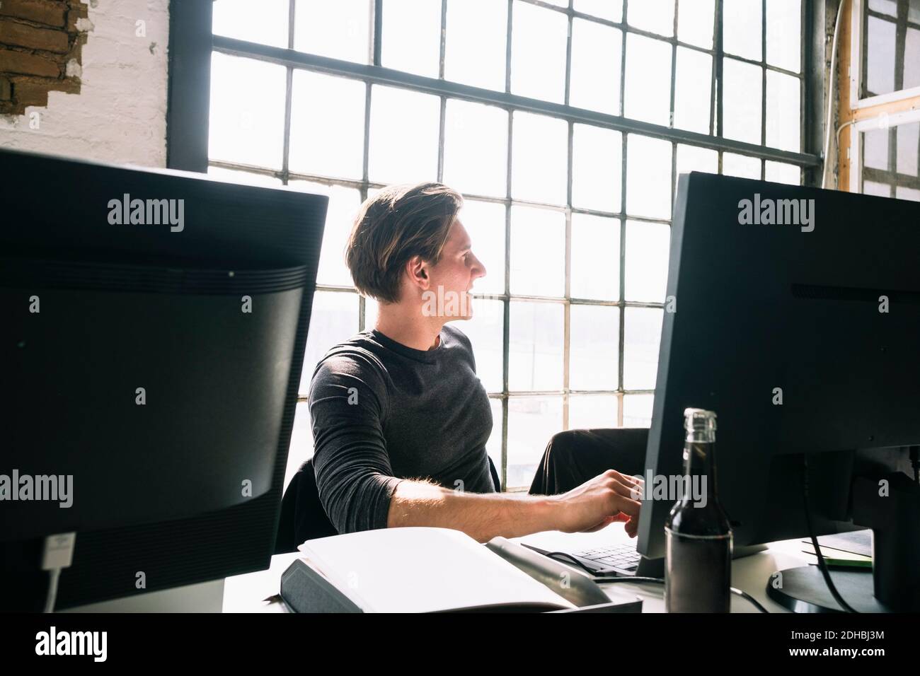 Junger männlicher Hacker schaut weg, während er am Computertisch sitzt Am kreativen Arbeitsplatz Stockfoto