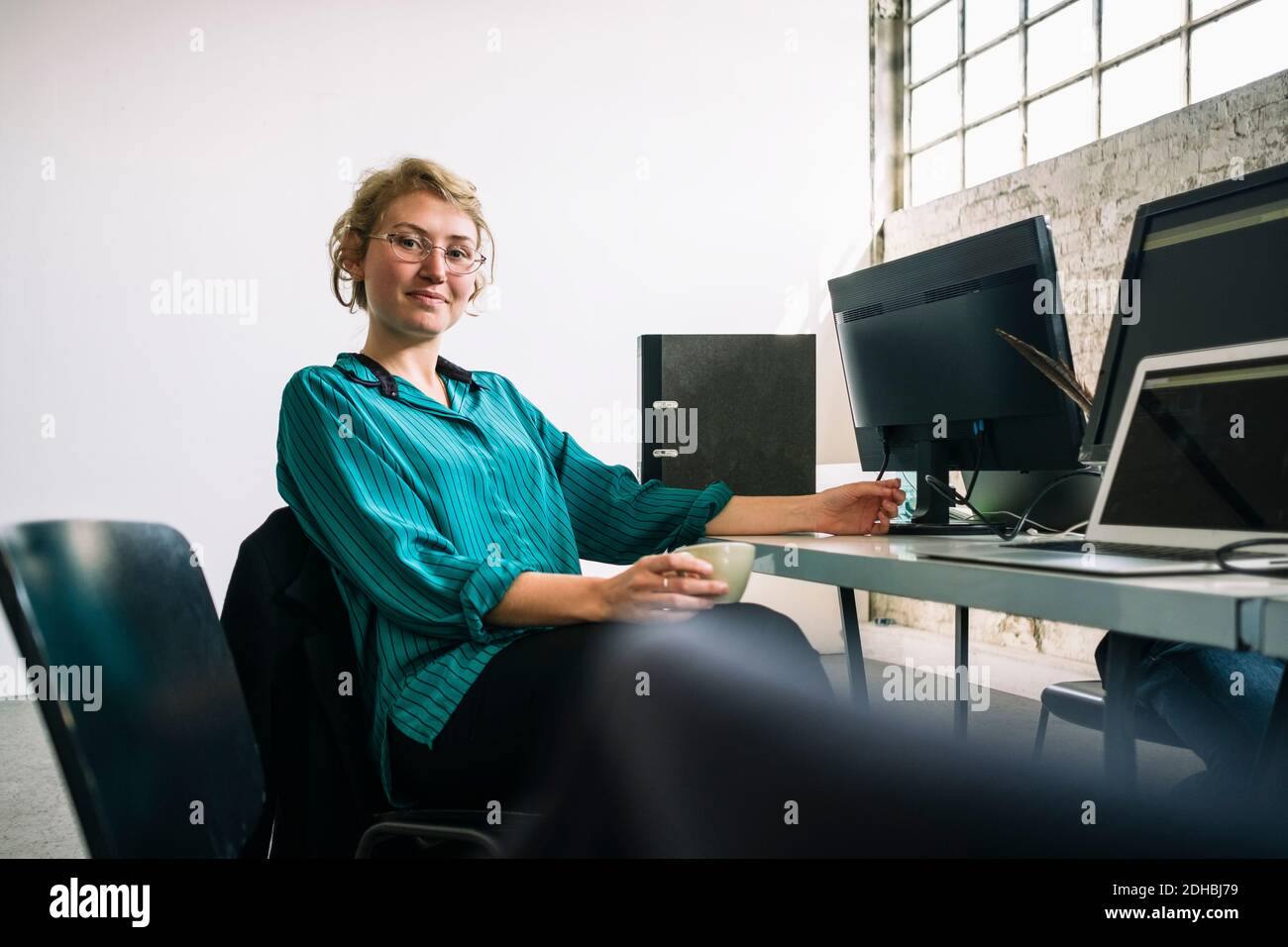 Porträt von selbstbewussten jungen Geschäftsfrau sitzen am Schreibtisch in kreativ Büro Stockfoto