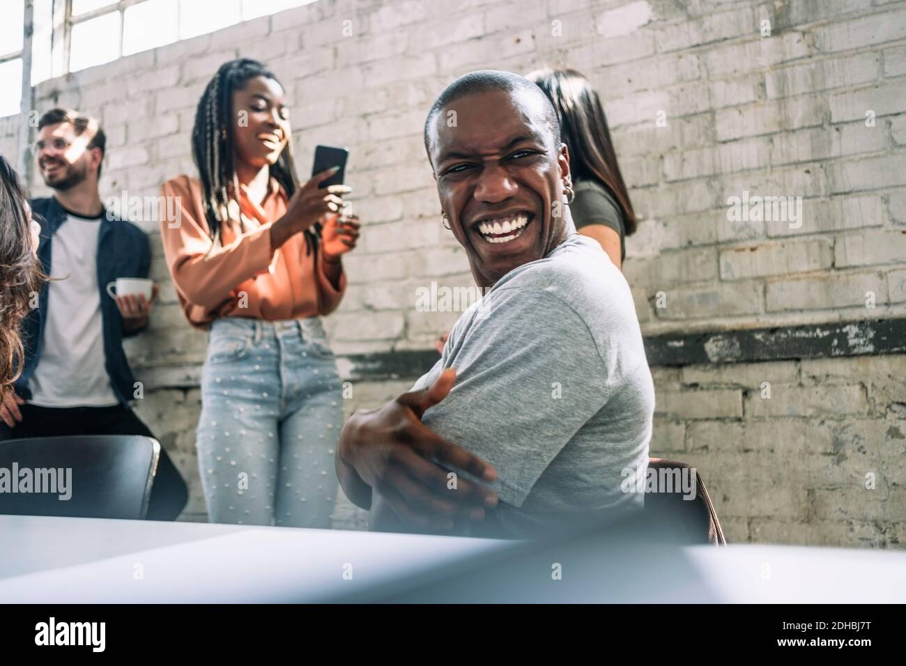 Fröhlicher junger Hacker, der über die Schulter schaut, während er im Hotel sitzt Konferenzraum im Kreativbüro Stockfoto