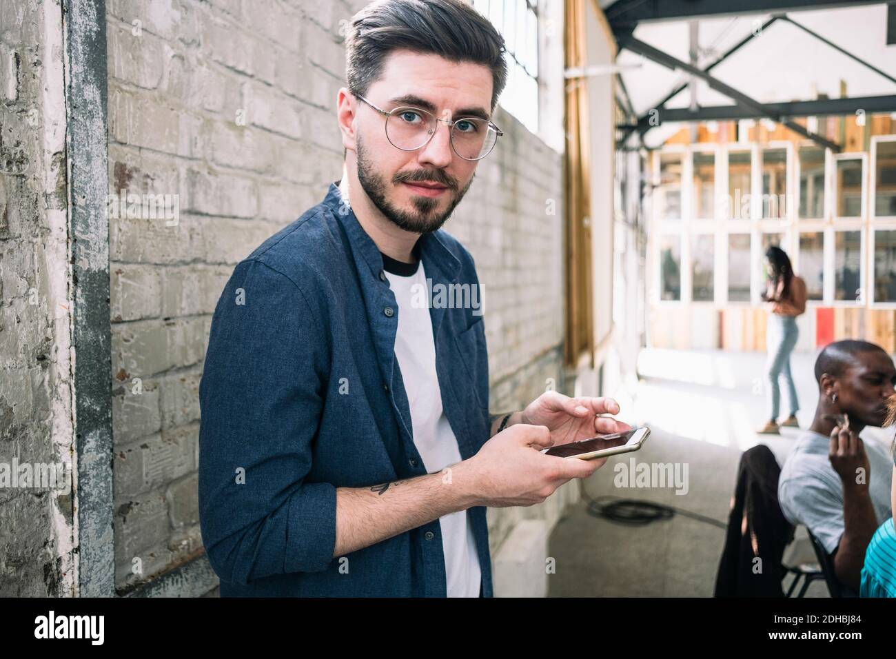 Porträt des selbstbewussten jungen Geschäftsmann stehen mit Smartphone gegen Ziegelwand am kreativen Arbeitsplatz Stockfoto