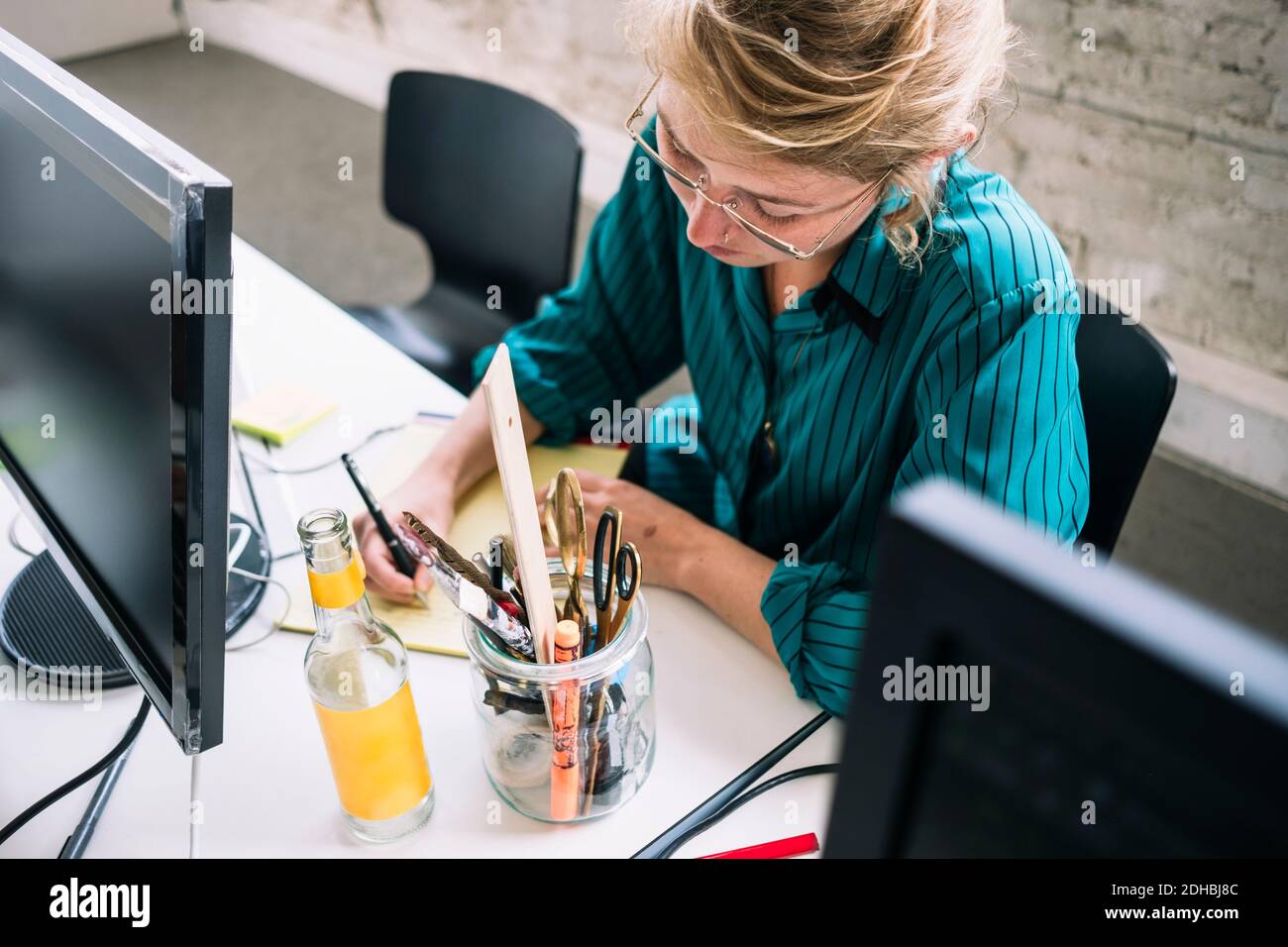 High-Angle-Ansicht der selbstbewussten weiblichen IT-professionellen Schreiben auf Notizblock am Schreibtisch im Kreativbüro Stockfoto