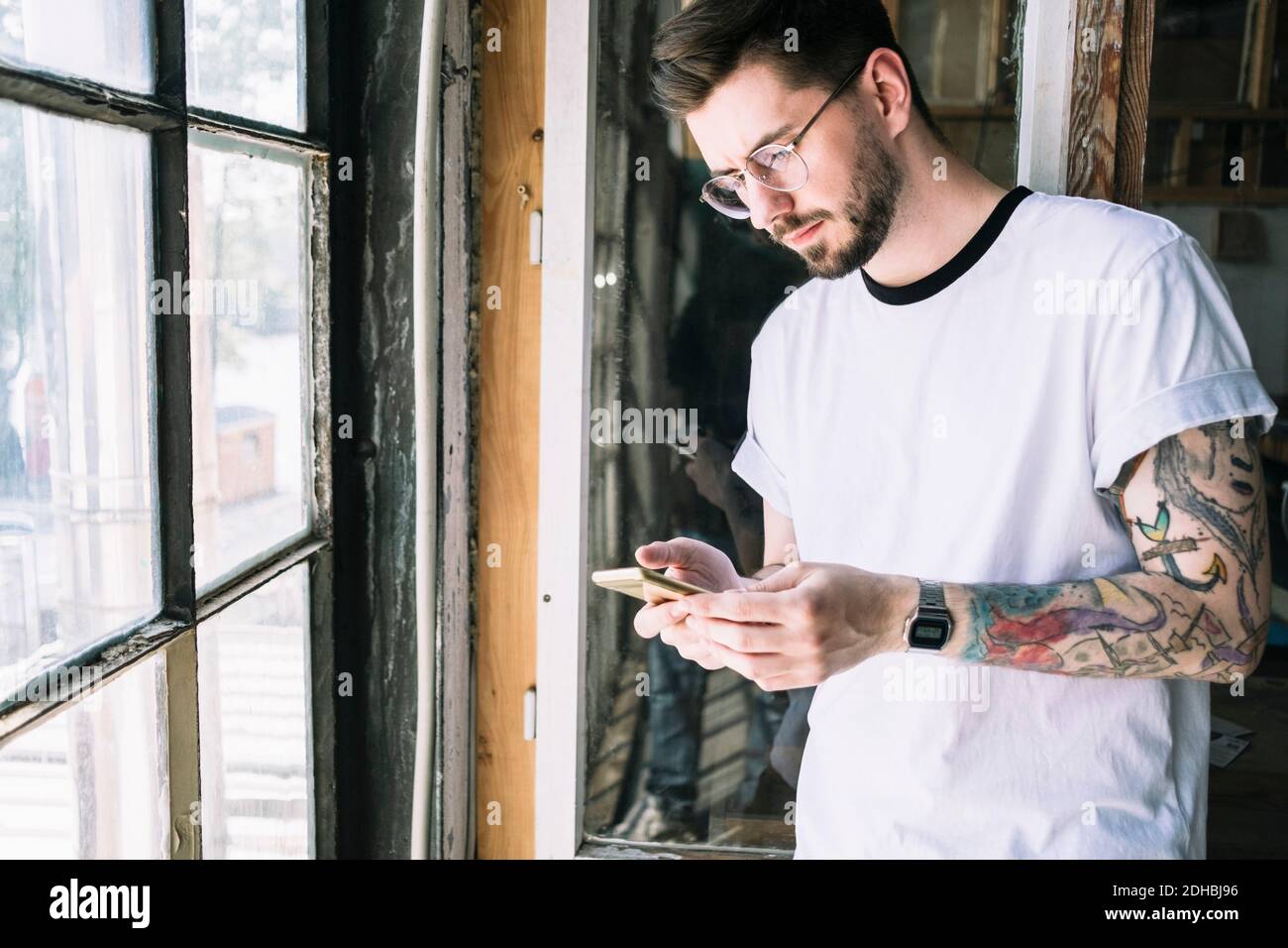 Zuversichtlich männlichen Hipster Hacker Textnachrichten durch Smartphone durch Fenster im Kreativbüro Stockfoto
