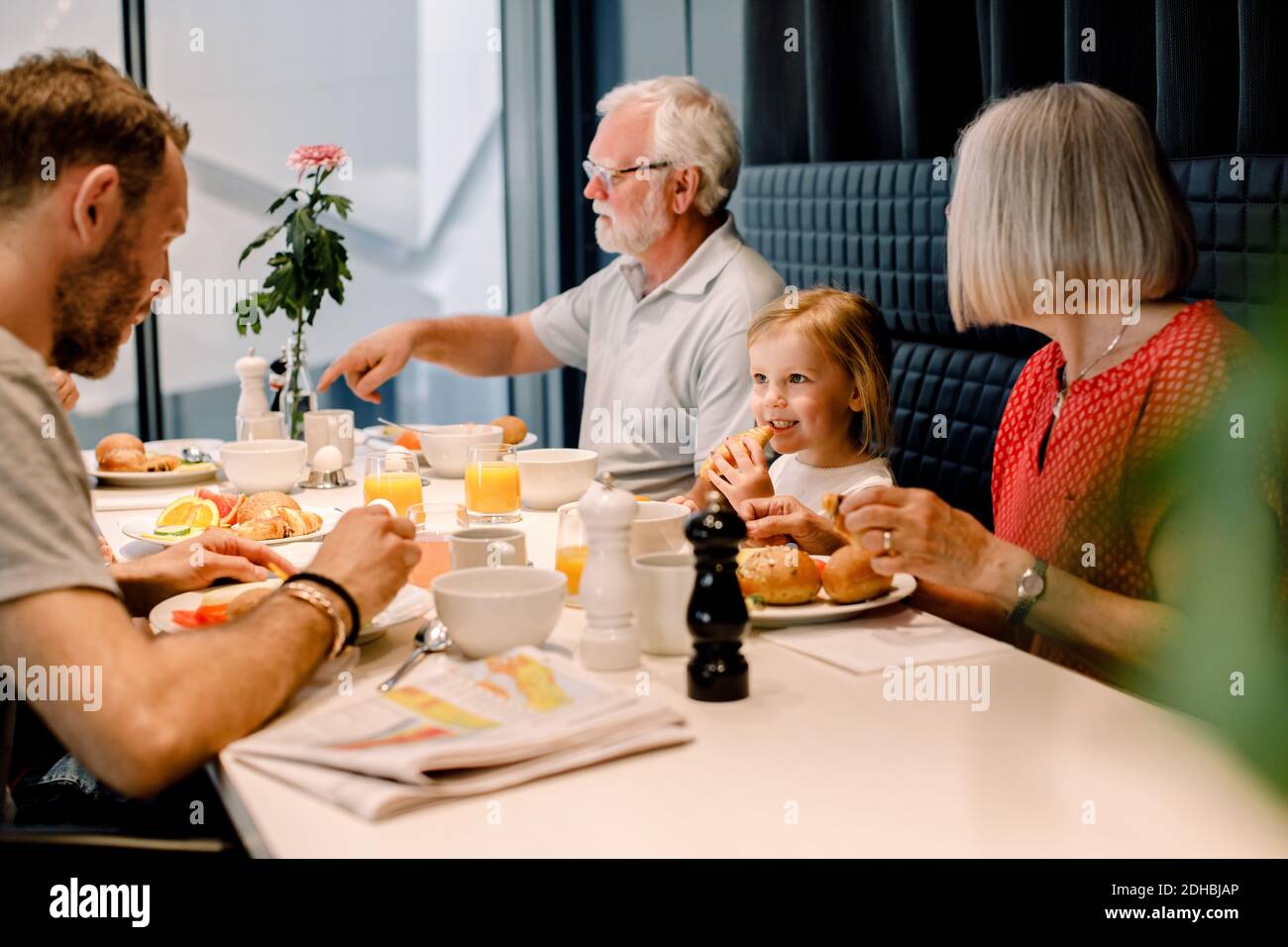 Lächelndes Mädchen, das Vater ansieht, während es mit Großeltern Essen hat Im Restaurant Stockfoto