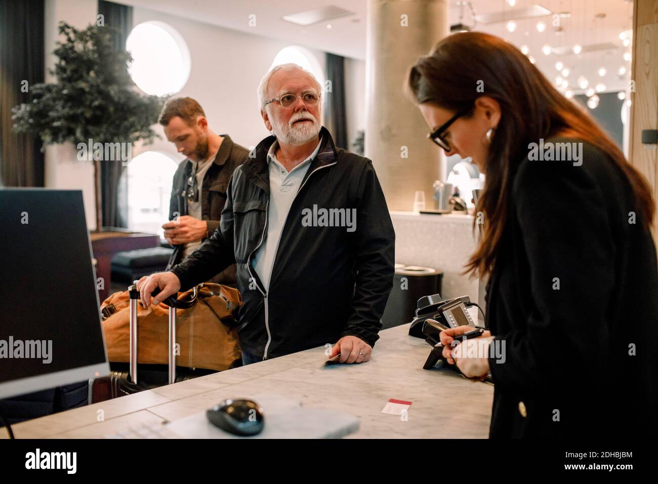 Ein älterer Mann schaute weg, während er mit dem Rezeptionisten stand Im Hotel Stockfoto