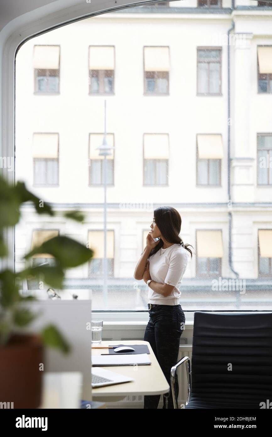 Seitenansicht der reifen Frau sprechen auf Handy, während Blick durch das Fenster im Büro Stockfoto