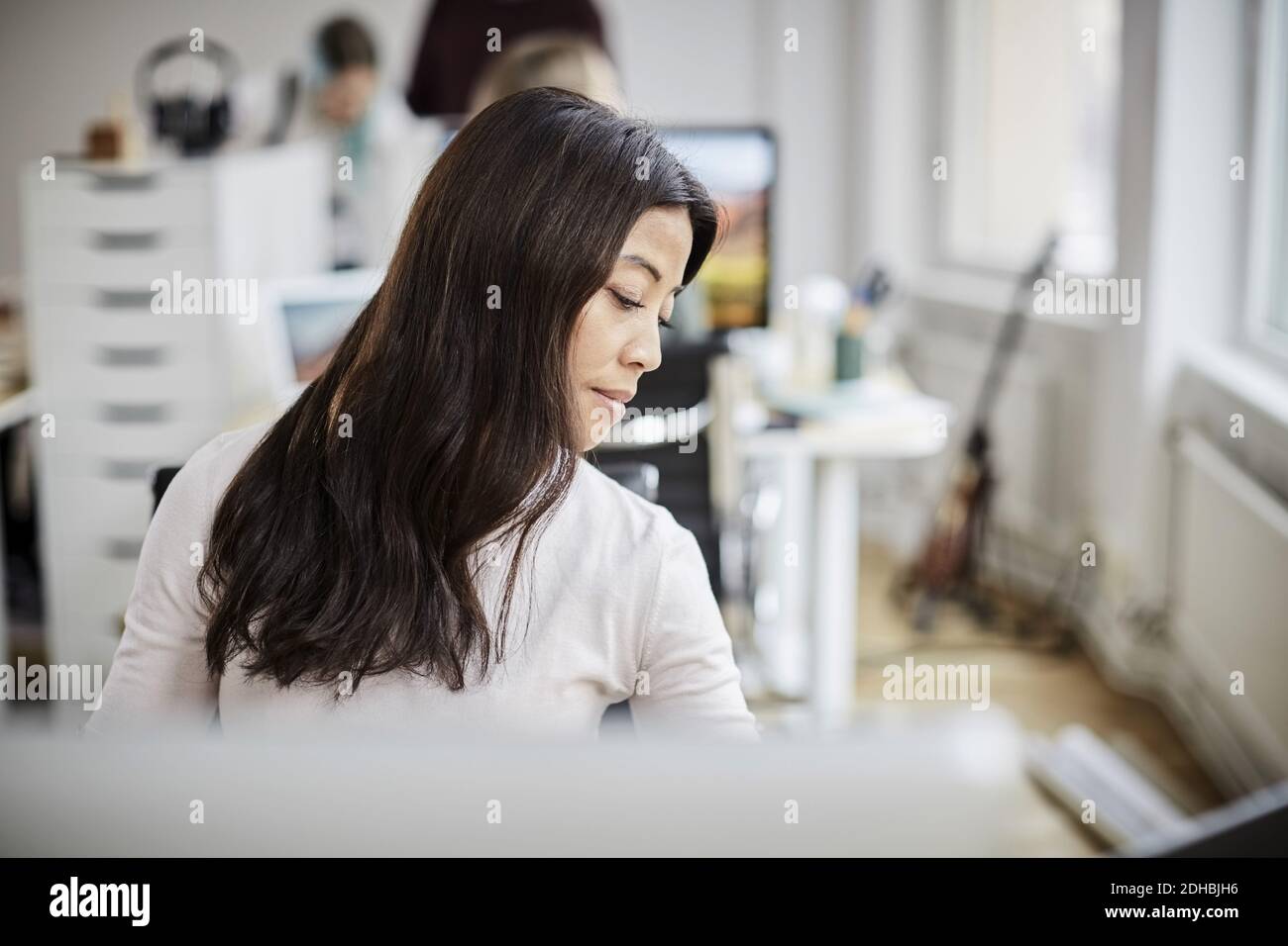 Eine reife Geschäftsfrau schaut nach unten, während sie im Büro am Schreibtisch sitzt Stockfoto