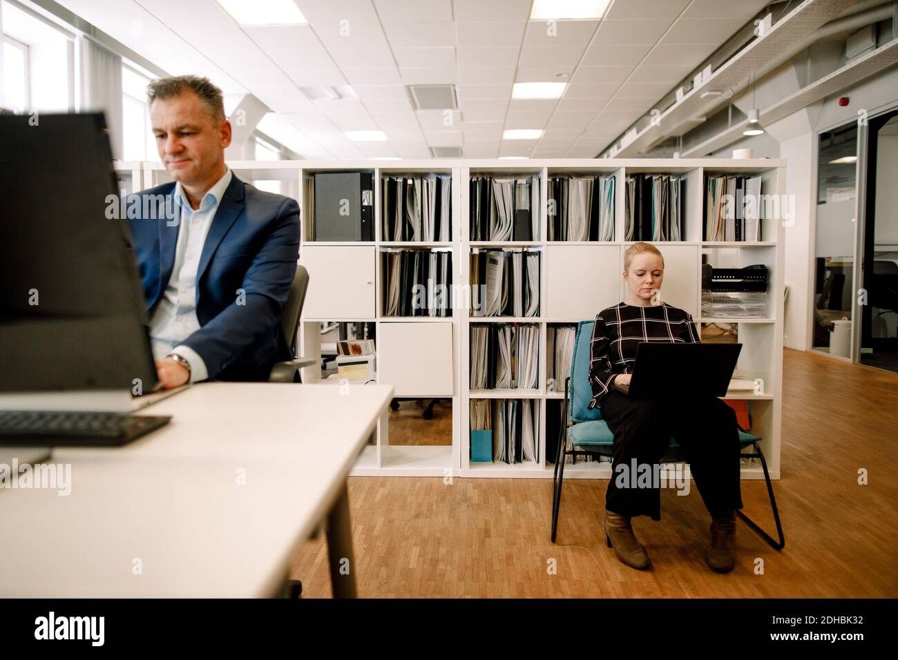 Reifer Geschäftsmann, der am Schreibtisch arbeitet, während eine Geschäftsfrau einen Laptop benutzt Büro Stockfoto