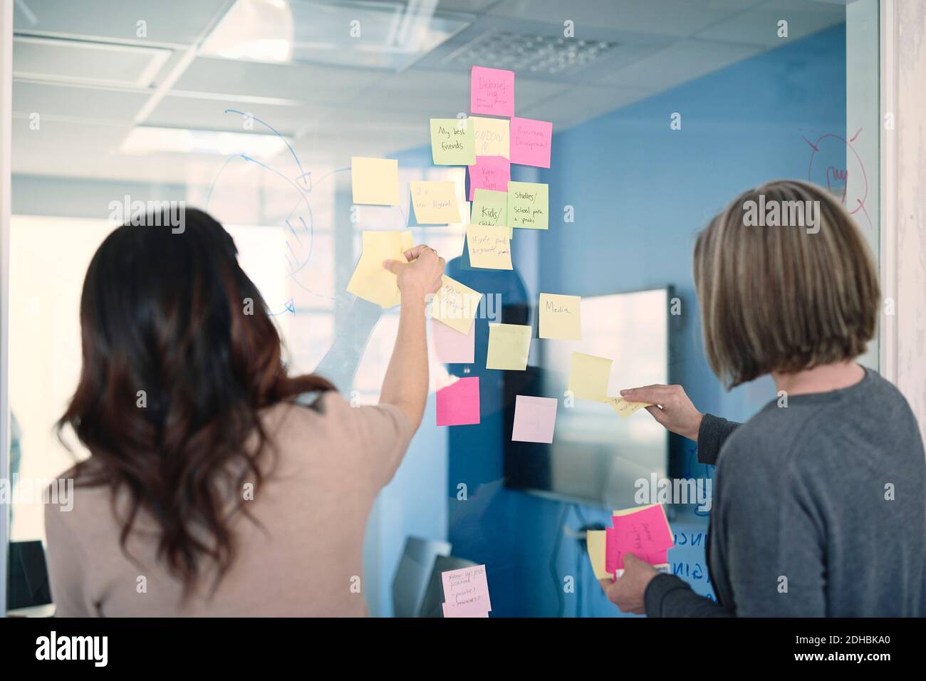 Geschäftsfrauen kleben Haftnotizen auf Glas im Büro Stockfoto