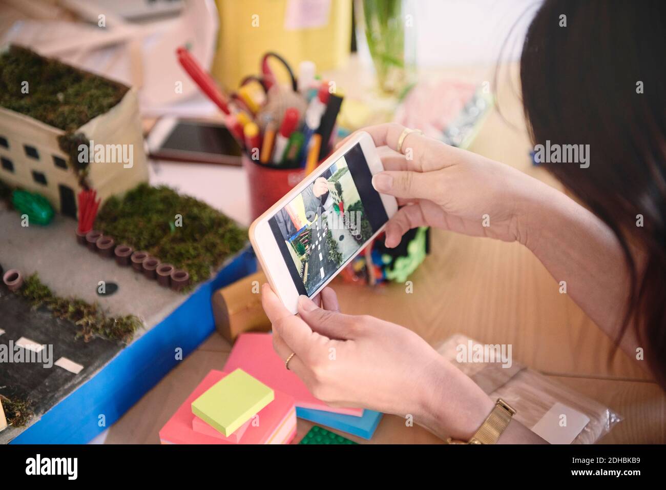 Zugeschnittenes Bild einer Ingenieurin beim Fotografieren eines Architekturmodells durch mobile Geräte Telefon am Tisch im Büro Stockfoto
