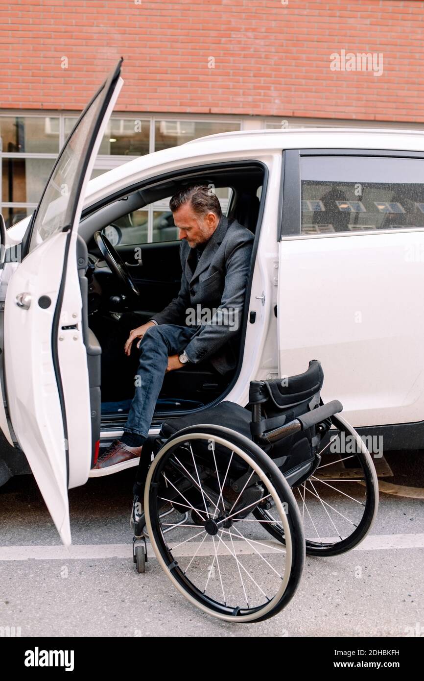 Volle Länge Seitenansicht der reifen Disable Mann Ausstieg aus Auto mit Rollstuhl auf der Straße in der Stadt Stockfoto