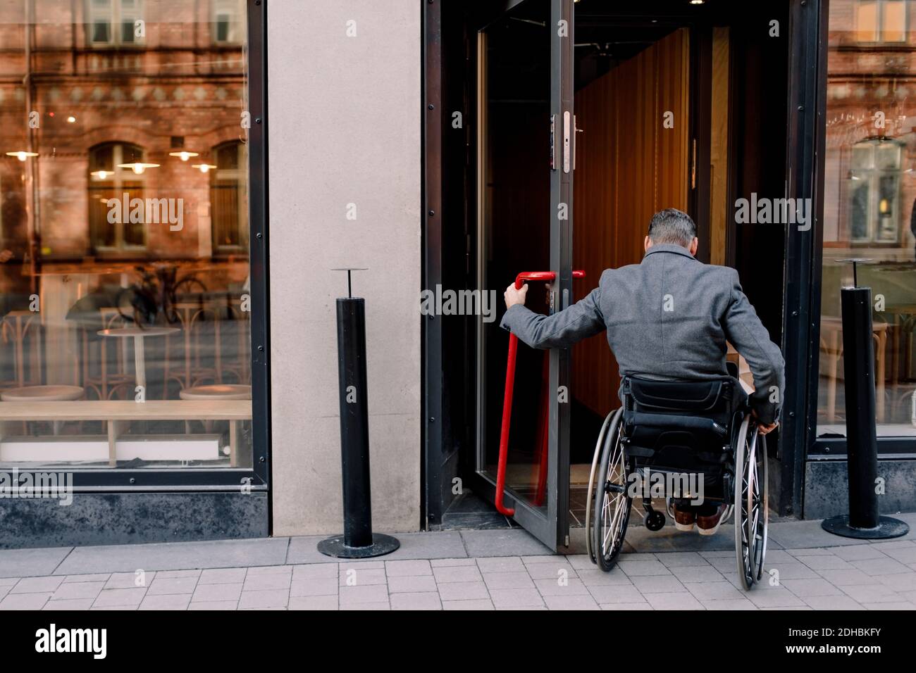Rückansicht des behinderten älteren Mannes, der auf dem Rollstuhl sitzt, während Im Geschäft betreten Stockfoto