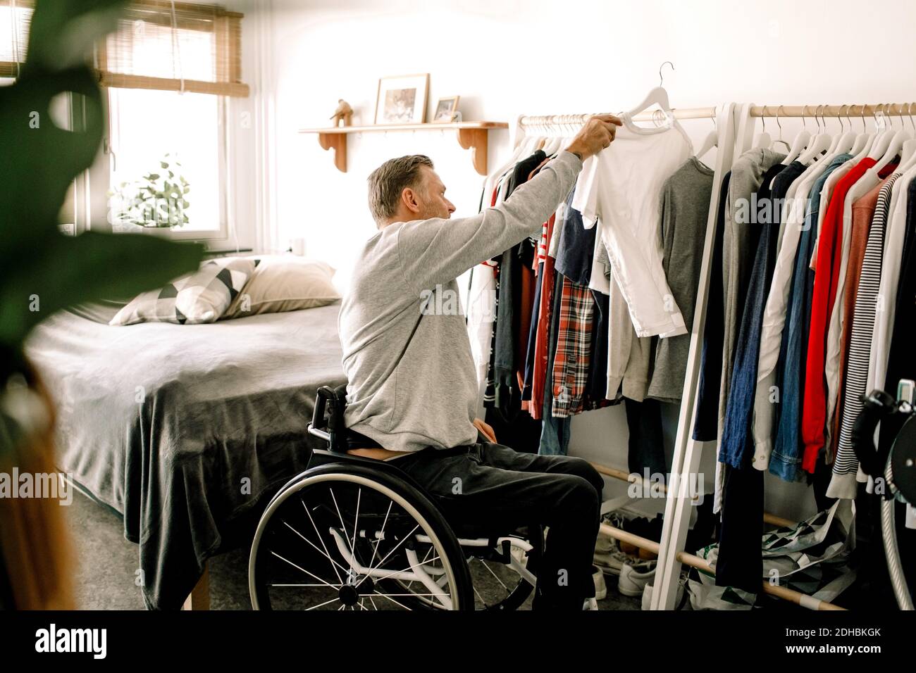 Seitenansicht des behinderten reifen Mannes, der weißes T-Shirt aufgehängt hat Kleiderständer zu Hause Stockfoto