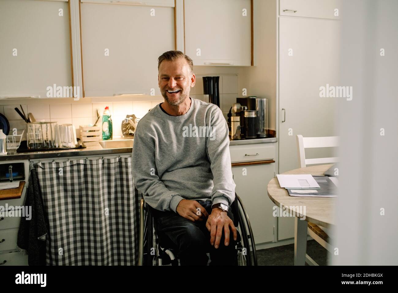 Fröhlicher reifer Mann sitzt auf Rollstuhl in der Küche zu Hause Stockfoto