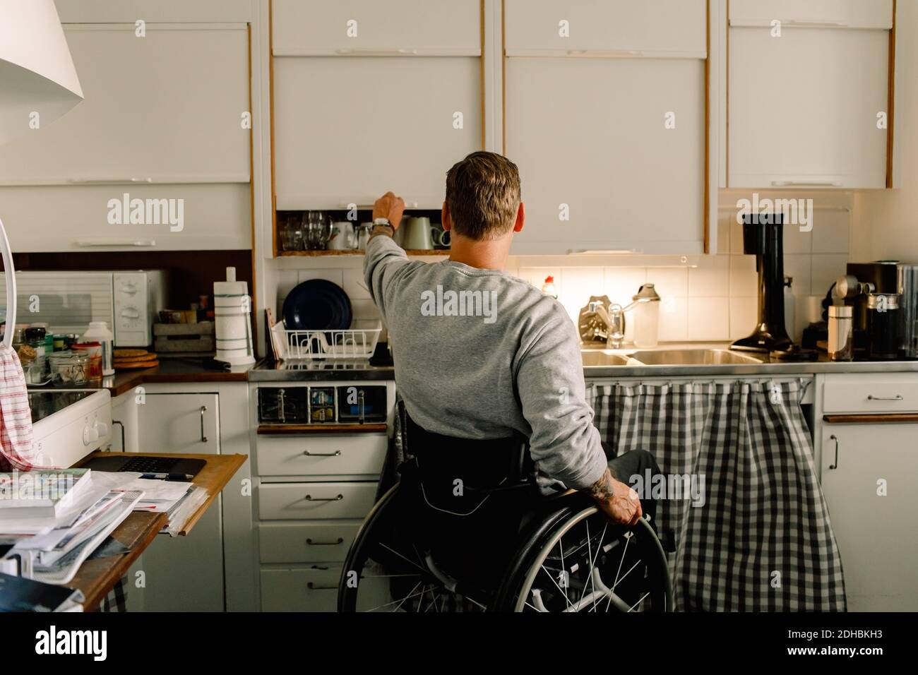 Rückansicht des behinderten Mannes, der den Schrank in der Küche öffnet Zu Hause Stockfoto