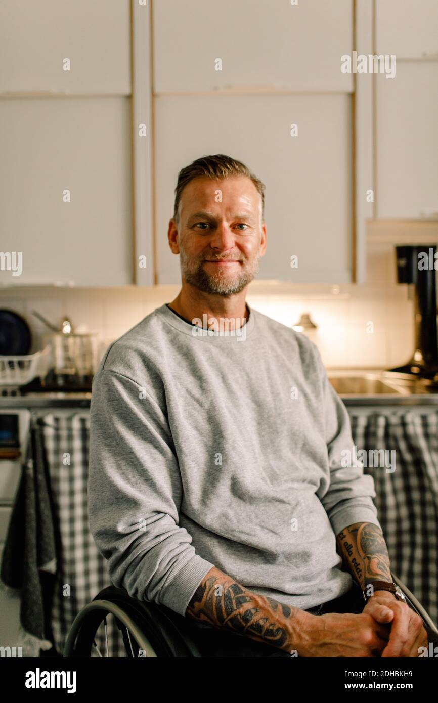 Porträt von selbstbewussten lächelnden behinderten Mann auf Rollstuhl sitzen in Küche zu Hause Stockfoto