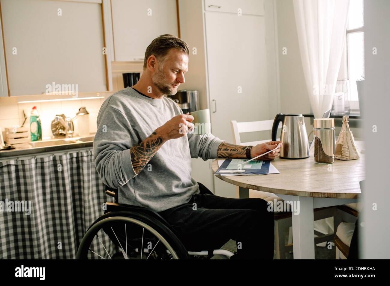 Tätowiert reifen Mann lesen Mail, während die Kaffeetasse auf Rollstuhl zu Hause Stockfoto
