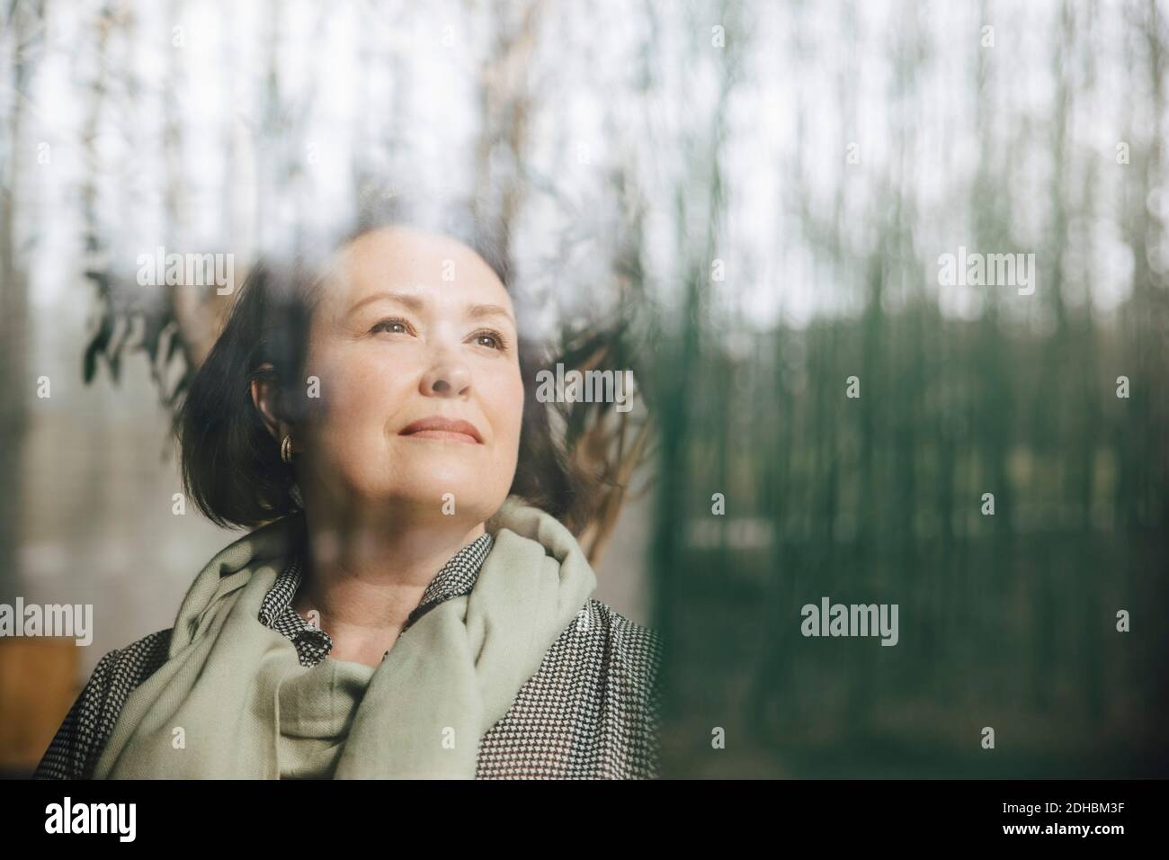 Durchdachte Geschäftsfrau, die durch das Fenster am Arbeitsplatz schaut Stockfoto